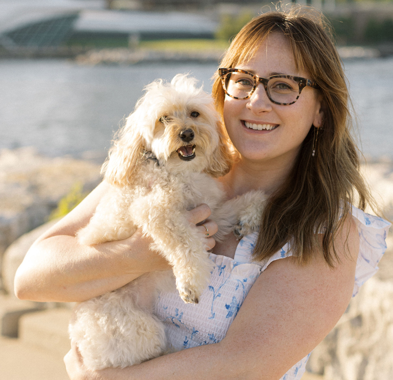 Monique and her little white dog, Wally, standing in front of a body of water.