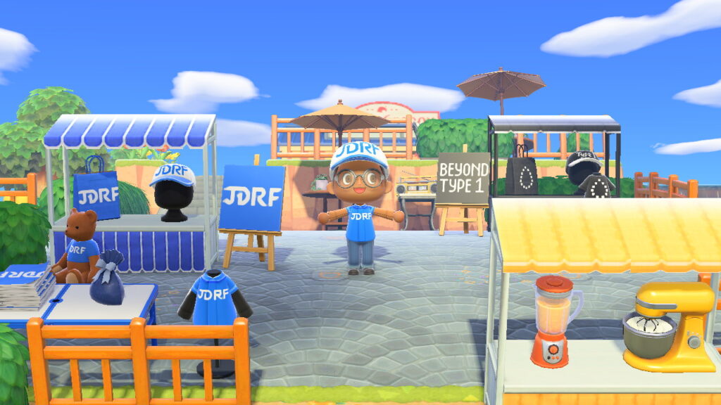 An Animal Crossing character wearing a Breakthrough T1D cap, posing near a booth with Breakthrough T1D merchandise and a teddy bear wearing a Breakthrough T1D shirt.