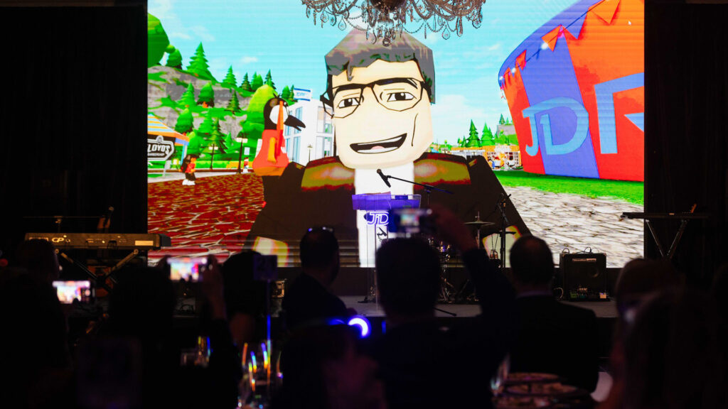 Aaron Kowalski's Roblox character on-screen in the background with silhouettes of people watching in the foreground.