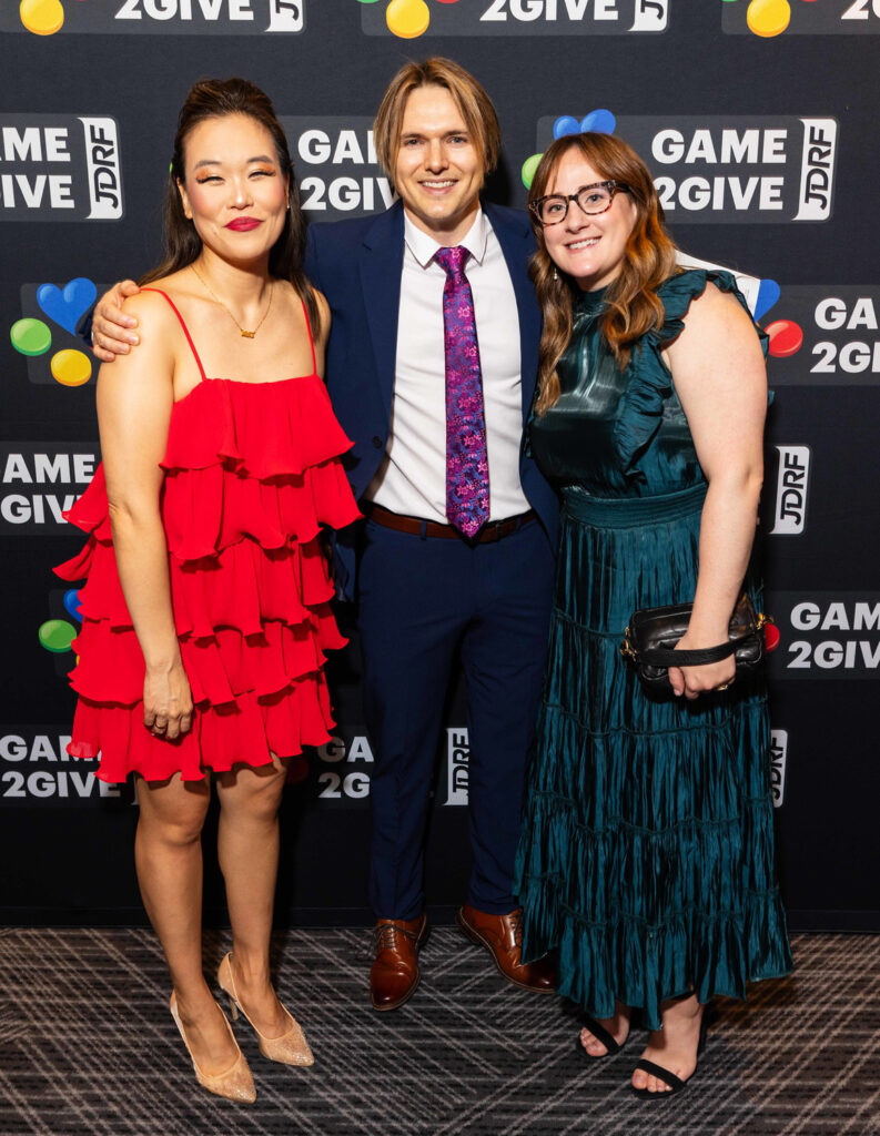 Three people in formal attire posing in front of a wall of Breakthrough T1D Play logos.