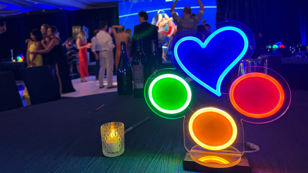 Lit-up neon sign of the Breakthrough T1D Play logo, with people dancing in the background.