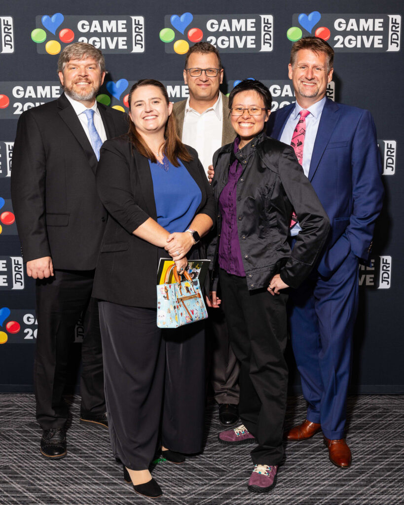 A group of people posing in front of a wall of Breakthrough T1D Play logos.